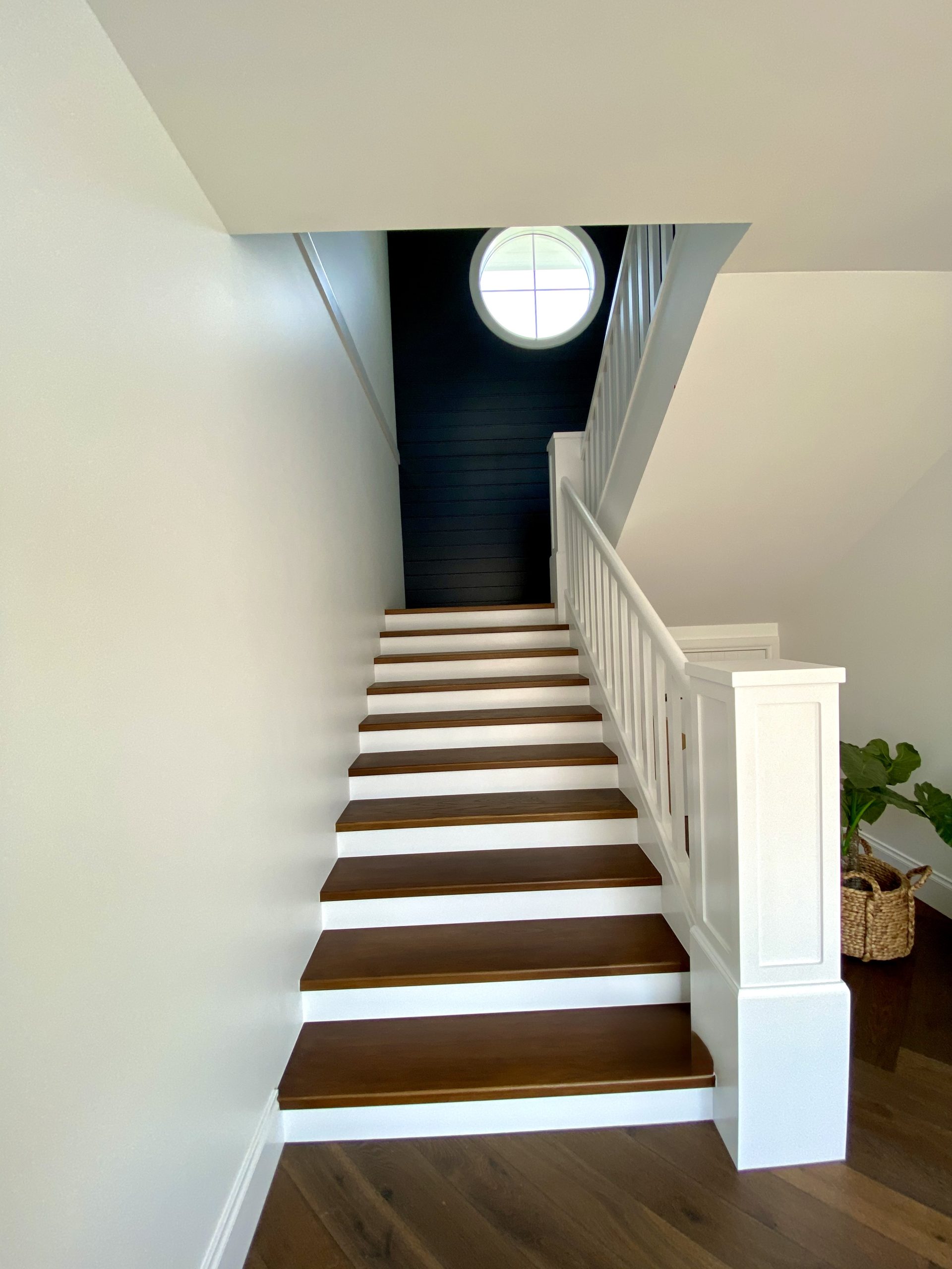 Timber staircase with white walls and balustrade beside a dark feature wall